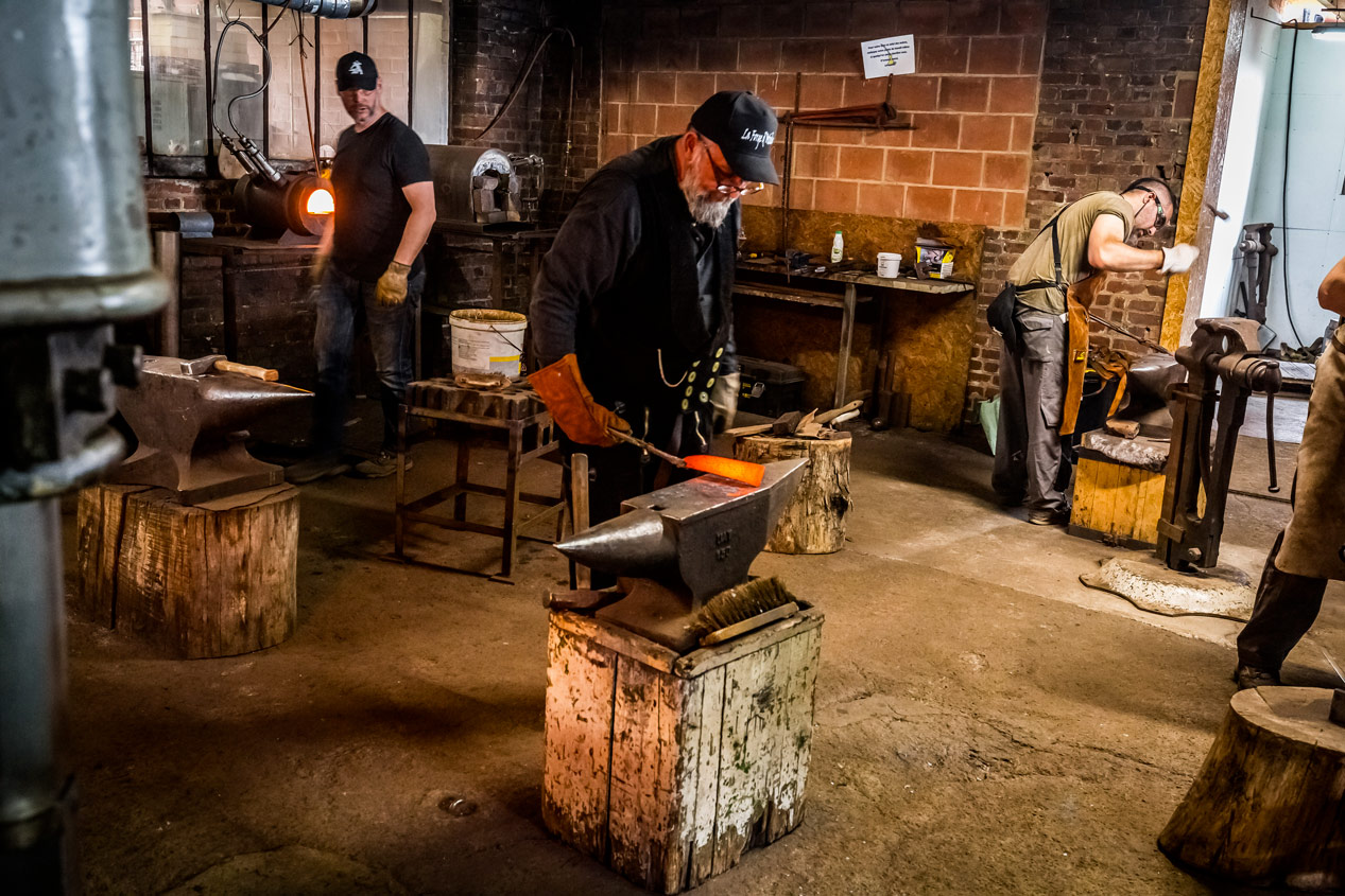 Vue d'ensemble de l'atelier de forge avec trois forgerons travaillant sur leurs enclumes