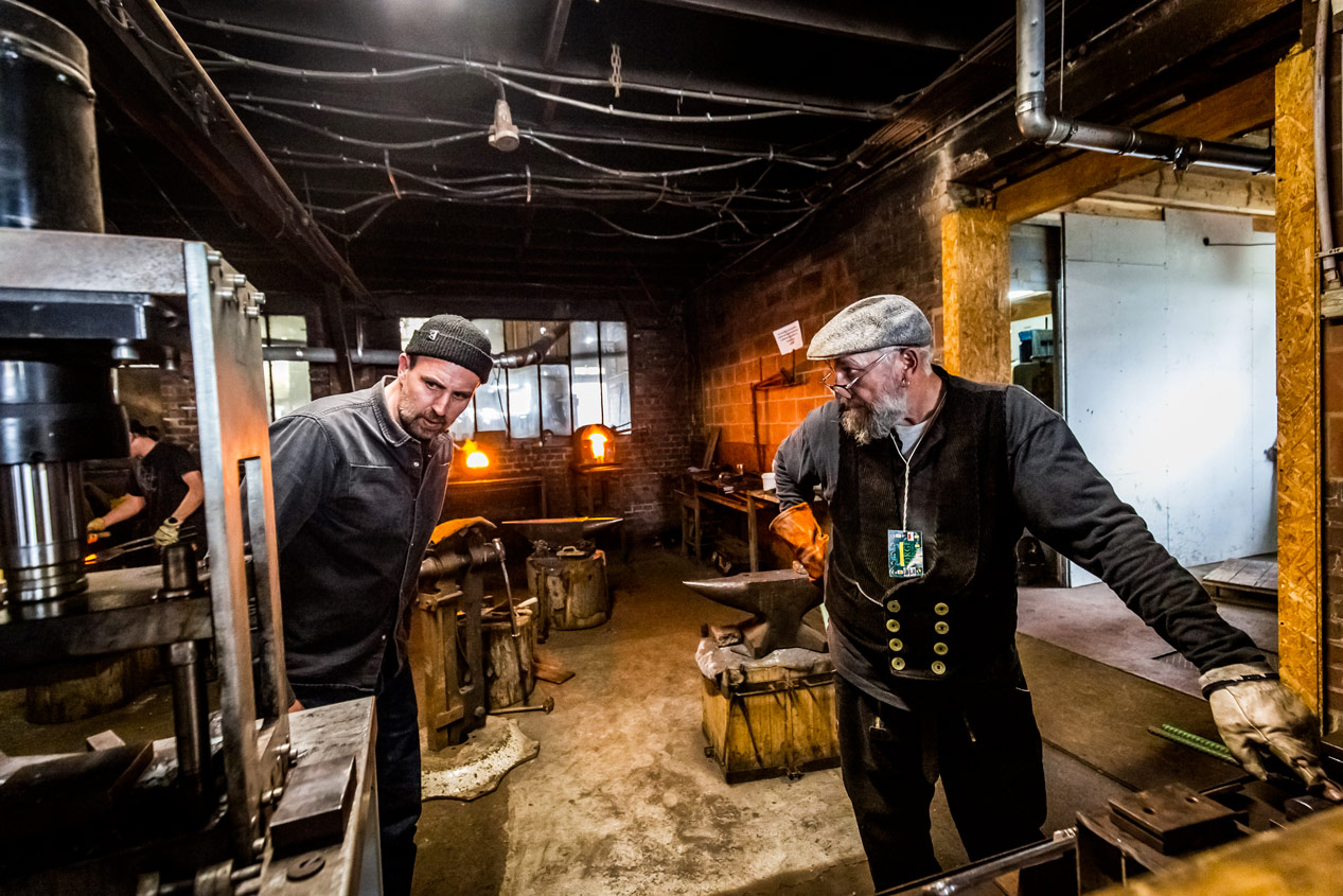 Deux forgerons discutant dans l'atelier, transmission du savoir